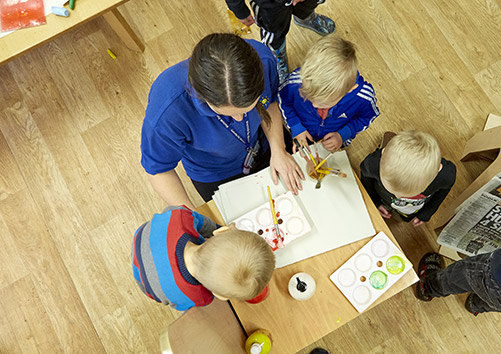nursery worker playing with children around a desk