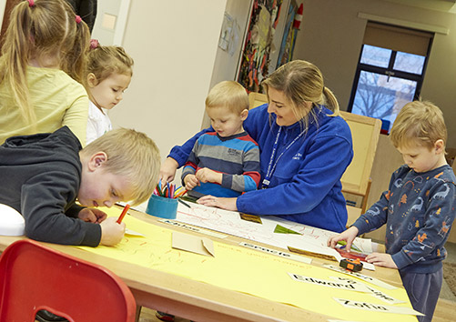 nursery worker drawing with children around a table